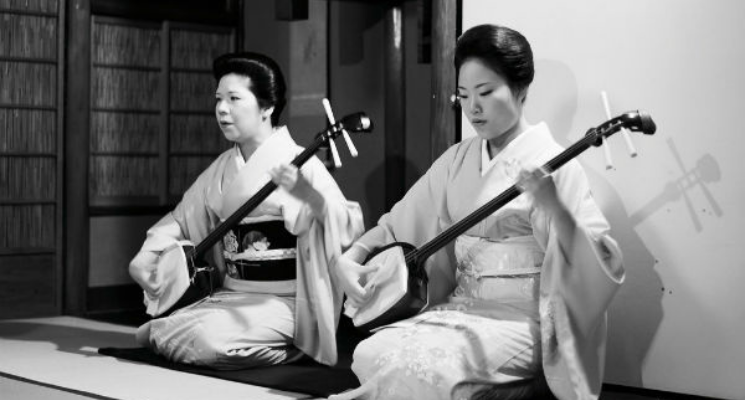Two women wearing traditional Japanese dress playing the Shamisen instrument